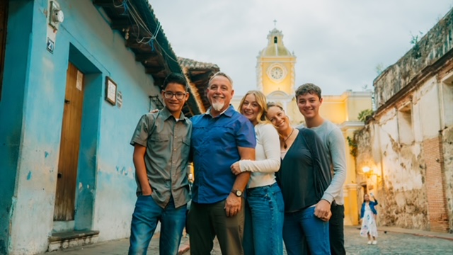 Family standing in between two buildings outside in another country.