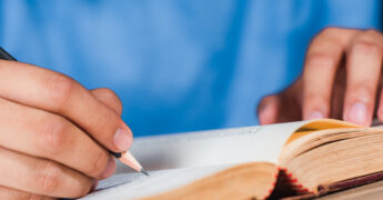 a man writing note with wooden pencil in old book