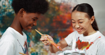two students smiling and painting