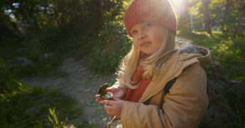 child outside in nature holding compass looking at camera